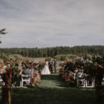 Two flowers on logs behind rows of chairs of an audience watching a couple get married