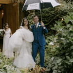 Bride and groom leaving the Barn as Groom holds an umbrella over them