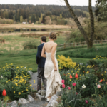 Groom leading his bride by the hand down a gravel path between tulips and yellow flowers