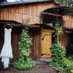 The front of the main Barn with doors shut, large bushes of ivy leaves and a white wedding dress hung from an upper overhang