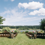 Wedding setup before guests arrive with two barrels of flowers behind rows of chairs overlooking a small lake