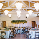 Circular tables for wedding guests with yellow flowers hanging from the ceiling and large inverted pyramid shaped lights