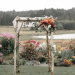 Closeup of a birch wedding arch with orange flowers tied to the top right corner