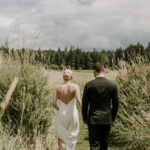 Bride and groom hand in hand walking through tall summer grass